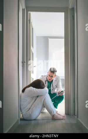 Psichiatra che parla con una paziente con disturbi mentali seduta sul pavimento in un centro di salute mentale Foto Stock