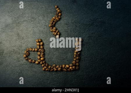 Piatto creativo con caffè su sfondo scuro. Tazza di caffè rivestita con chicchi di caffè torrefatti Foto Stock