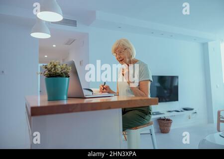 Donna anziana che guarda lo schermo del laptop in ambienti chiusi Foto Stock