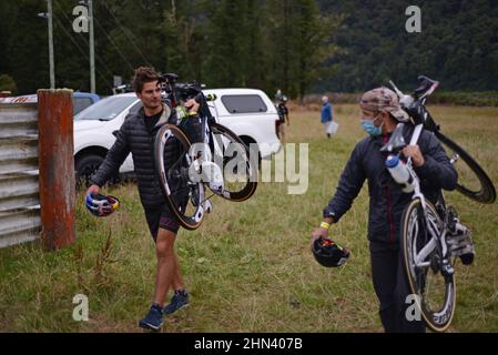 AICKENS, NUOVA ZELANDA, 12 FEBBRAIO 2022; un membro del team di supporto, a sinistra, porta la bicicletta per Braden Currie, il vincitore della sezione maschile elite del Triathlon Coast to Coast Foto Stock