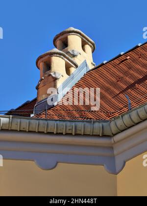 Tetto in piastrelle rosse e due camini in un edificio storico contro il cielo blu a Bratislava, Slovacchia. Foto Stock