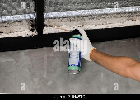 La mano umana nel guanto bianco sta cianfrinando le perdite del tetto con la schiuma di caulk inscatolata. Foto Stock