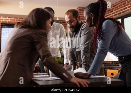 Diversi uomini d'affari si levano in piedi in su analizzando le idee di brainstorming del grafico di vendita per il progetto di partnership che lavora alla presentazione dell'azienda nell'ufficio di startup. Dirigenti che hanno riunioni di lavoro Foto Stock
