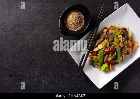 Manzo, verdure e semi di sesamo in piatto bianco su sfondo nero Foto Stock