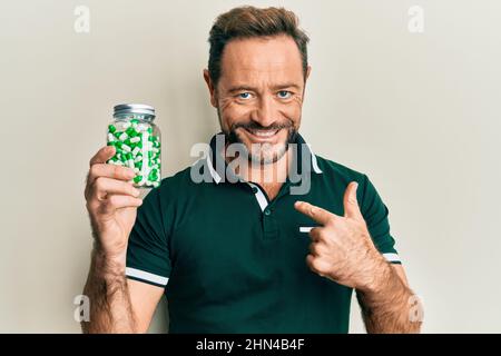 Uomo di mezza età che tiene le pillole puntando il dito ad un auto sorridente felice e orgoglioso Foto Stock