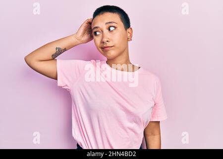 Bella donna ispanica con capelli corti indossando casual t shirt rosa confondersi e domandarsi. Incerto con dubbio, pensando con mano Foto Stock