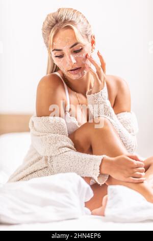 La ragazza buona-osservante applica il prodotto di pulizia di skincare sul suo viso in camera da letto. Foto Stock