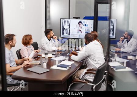 Un grande gruppo di esperti medici multietnici in laboratori che ascoltano i colleghi che condividono nuove informazioni durante una riunione online Foto Stock