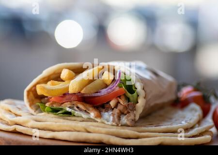 Cibo di strada greco Gyros da portare via, ben avvolto con pomodoro, souvlaki, insalata greca, cipolla e patatine fritte Foto Stock