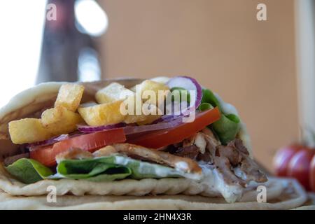 Cibo di strada greco Gyros da portare via, ben avvolto con pomodoro, souvlaki, insalata greca, cipolla e patatine fritte Foto Stock