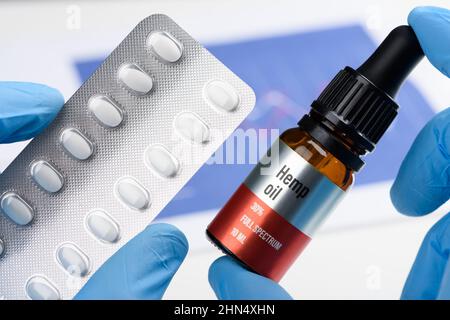 Lo scienziato tiene e confronta l'olio di canapa CBD in una mano e blister di pillole in un'altra. Concetto alternativo di ricerca di trattamento di medicina naturale. Foto Stock