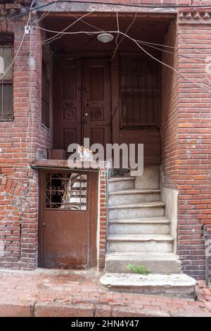 Vecchia porta in casa di mattoni con scala in cemento usurata e un ingresso al seminterrato. Molti fili. Foto Stock