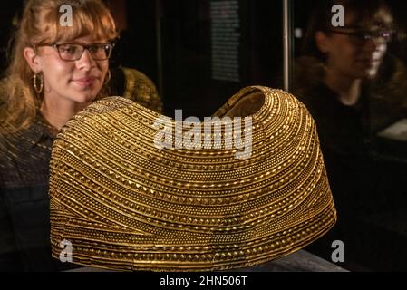 Londra, Regno Unito. 14 febbraio 2022. Un membro dello staff pone con un mantello d'oro di Mold in Galles, circa 1900-1600 a.C. Anteprima di “il mondo di Stonehenge” al British Museum”, la prima grande mostra del Regno Unito a Stonehenge che presenta oltre 430 oggetti in mostra da Gran Bretagna, Irlanda ed Europa. I lavori sono esposti dal 17 febbraio al 17 luglio 2022. Credit: Stephen Chung / Alamy Live News Foto Stock