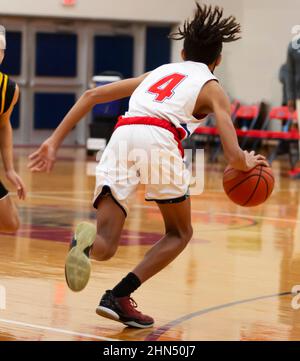 Il giocatore di basket che dribbling la palla e fare una nove sul suo difensore durante una partita di basket al coperto di scuola superiore. Foto Stock