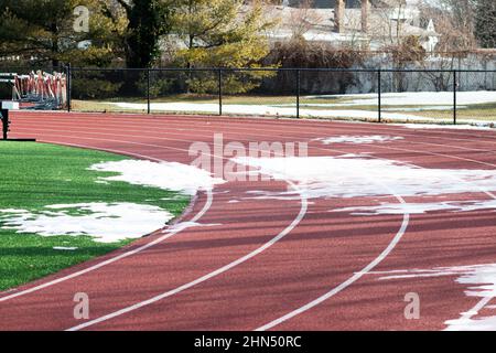 Una pista di scuola superiore ha ancora neve e ghiaccio al primo turno, come il resto della neve si è sciolto. Foto Stock