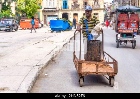 Un uomo afro-caraibico spinge un carrello in una strada della città. Sullo sfondo si vedono un bicitaxi e una spazzatura. Foto Stock