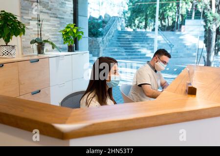 Due receptionist che indossano maschere per il viso nel centro di fisioterapia Foto Stock