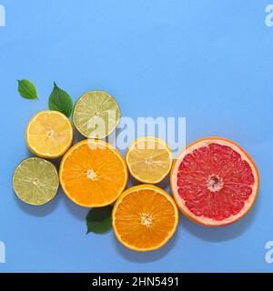 Scena estiva con vari agrumi a fette e foglie verdi su sfondo ciano o blu. Spazio per la copia creativa Flat Lay Foto Stock