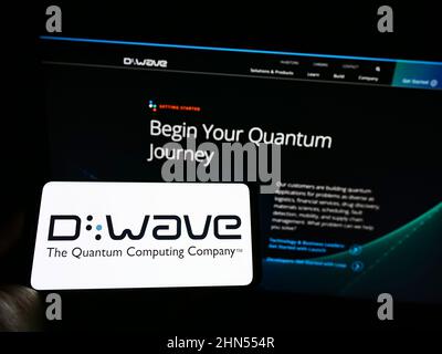 Persona che tiene il cellulare con il logo della società canadese di hardware D-Wave Systems Inc. Sullo schermo di fronte al sito web aziendale. Mettere a fuoco sul display del telefono. Foto Stock