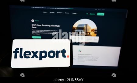 Persona che detiene il cellpohone con il logo della società di logistica statunitense Flexport Inc. Sullo schermo di fronte al sito web aziendale. Mettere a fuoco sul display del telefono. Foto Stock