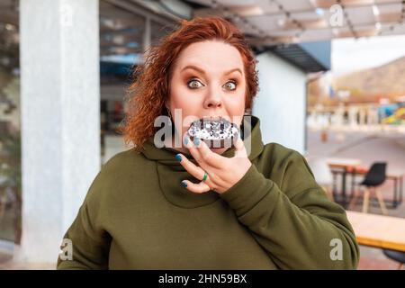 Ritratto di più grande meraviglia donna mangiare una ciambella di cioccolato. Il concetto di dieta e nutrizione. Foto Stock