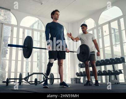 sollevamento pesi per atleta diversamente abile con il suo allenatore in palestra. Uomo con gamba protesica che viene allenato dal suo allenatore Foto Stock