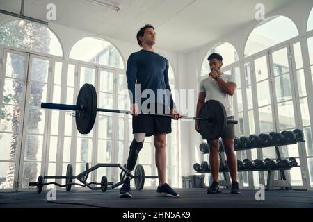 Paralimpico atleta sollevamento pesi con il suo allenatore in palestra. Uomo con gamba protesica che viene allenato dal suo istruttore Foto Stock