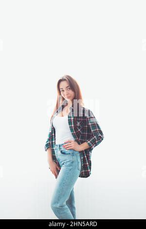 Ritratto di una giovane donna bruna sottile in abiti casual che posa su sfondo bianco. Dietro il bagliore. Verticale. Spazio di copia. Foto Stock