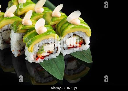 Tradizionale e delizioso sushi roll fresco su sfondo nero con riflessi. Sushi roll con riso, nori, formaggio cremoso, caviale tobiko, avocado. Dom Foto Stock