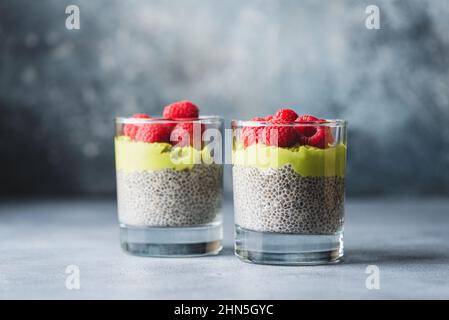 Budino Chia con lamponi e mousse di avocado in un bicchiere su tavola di cemento. Pasto vegano sano senza glutine per dieta, perdita di peso, Foto Stock