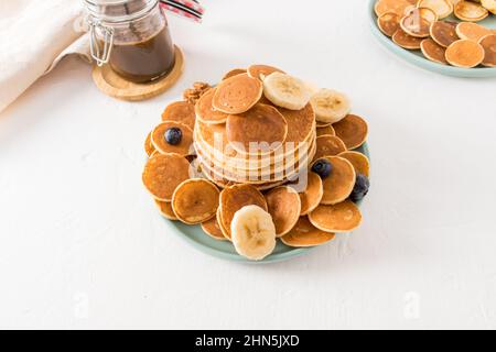 un assortimento di pancake su un piatto, pasta di cioccolato in un vaso su un tavolo bianco. deliziosa colazione per i bambini. sfondo bianco Foto Stock