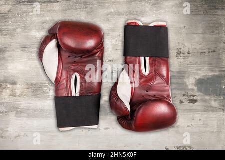Vista dall'alto dei guanti da boxe in pelle rossa vintage posizionati sulla superficie in legno grigio resistente agli agenti atmosferici