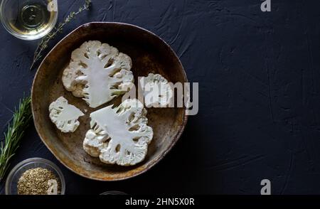 bistecca di cavolfiore, ricetta. Le parti grezze del cavolfiore si trovano in una padella. Vicino olio d'oliva, spezie. Sfondo scuro. Posiziona per testo. Foto Stock