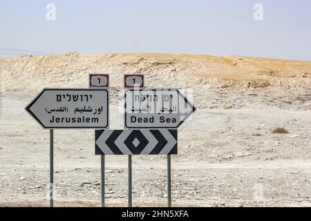 I cartelli stradali trilingui stampati in ebraico, arabo e inglese lungo l'autostrada 1 nel deserto della Giudea dirigono i viaggiatori verso Gerusalemme e il Mar Morto. Foto Stock