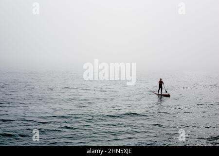 SUP, Standup paddleboarding, uomo solitario che galleggia nella nebbia Foto Stock