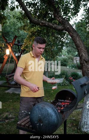 Bel maschio che prepara barbecue all'aperto. Salsicce fresche e hot dog grigliati Foto Stock