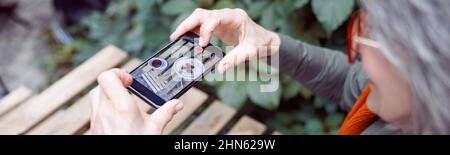 Ospite anziano scatta foto del dessert alle fragole con smartphone al tavolo all'aperto Foto Stock