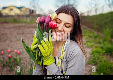 Il giardiniere ha raccolto il bouquet di tulipani freschi nel giardino primaverile. Giovane donna felice sorridente che tiene fiori. Primo piano verticale Foto Stock