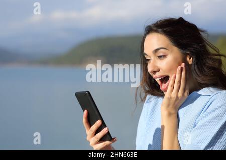 Stupito donna che controlla il telefono cellulare in un lago in vacanza Foto Stock