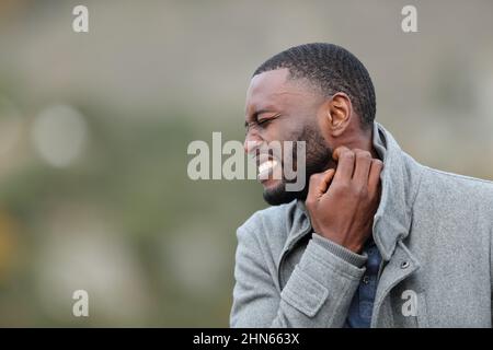 Uomo stressato con pelle nera che graffia il collo itchy in inverno in un parco Foto Stock