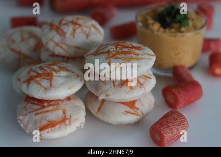 Carota folle e chutney di cocco. Torte di riso al vapore con carote grattugiate servite con condimenti piccanti al cocco. Scatto su sfondo bianco Foto Stock