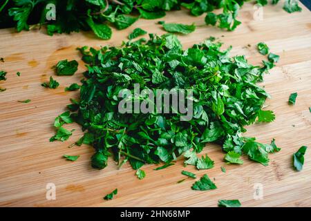 Erbe fresche tritate su un tagliere di bambù: Un mucchio di menta tritata, coriandolo e prezzemolo su un tagliere di legno Foto Stock