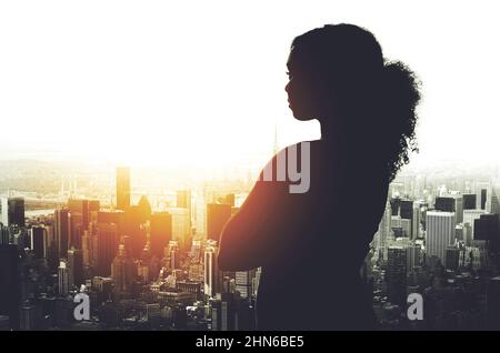 Il suo successo è stato plasmato in questa città. Un'immagine silhouetted di una giovane donna d'affari che guarda un paesaggio urbano da una finestra d'ufficio. Foto Stock