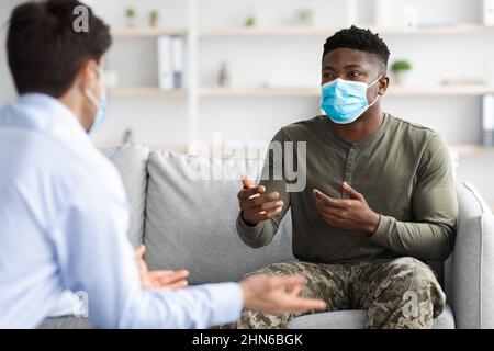 Soldato nero in maschera facciale visita psicologo mentre pandemico Foto Stock