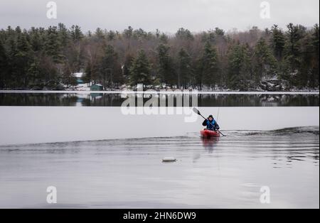 Teen boy pagaiare un kayak da pesca su un lago ghiacciato in inverno. Foto Stock