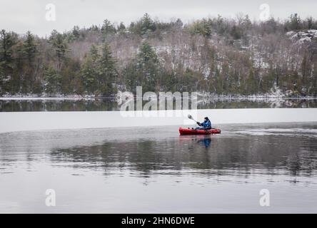 Teen boy pagaiare un kayak da pesca su un lago ghiacciato in inverno. Foto Stock