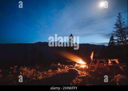 Seduti attorno al fuoco nelle montagne della Cascade del Nord di notte Foto Stock