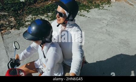 Due donne turistiche caucasiche guida uomo su scooter rosso. Fai selfie. Coppia d'amore in moto in abiti bianchi per andare sulla foresta strada percorso viaggio. Motocicletta affitto casco di sicurezza occhiali da sole. Giro turistico. Foto Stock