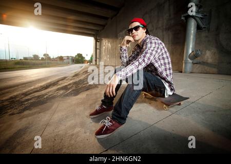 Skateboarder seduto a bordo sotto il cavalcavia Foto Stock