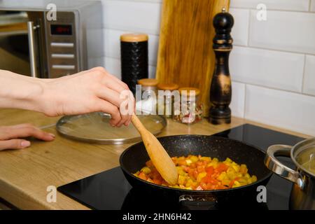 Primo piano di una mano femmina mescolando le verdure tritate in una padella con spatola di legno. Processo di preparazione del sugo di verdure. Foto Stock